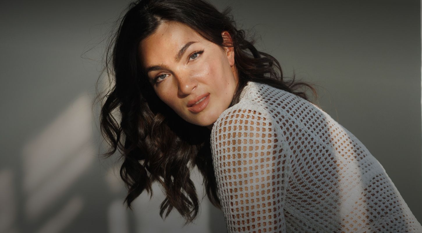 Woman with wavy hair in white knit top.
